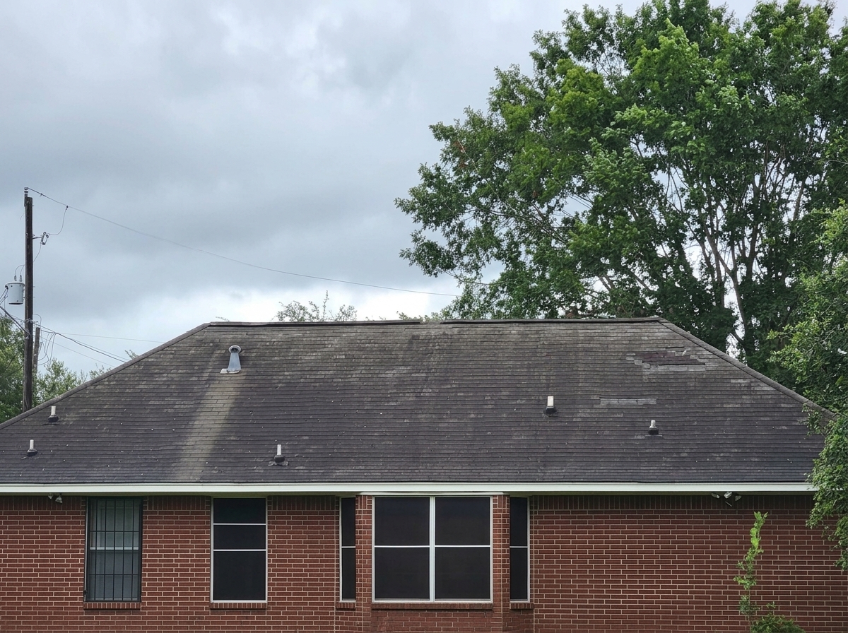 Front view of a single story brick house showing heavy shingle wear and roof discoloration before construction begins
